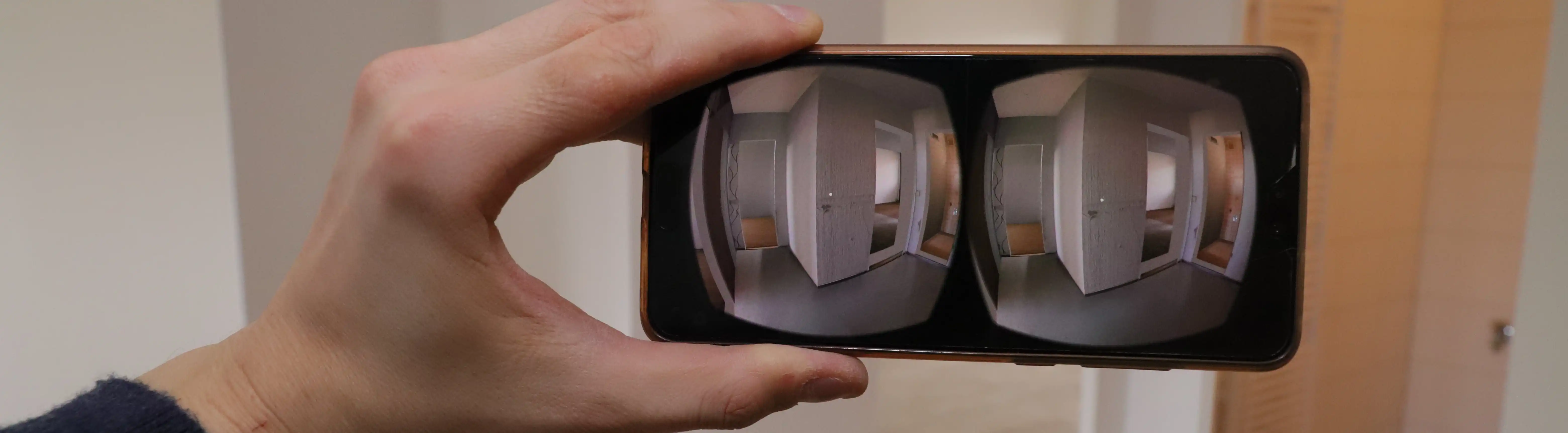 Nahaufnahme eines Smartphones in einer VR-Halterung: Auf dem geteilten Stereo-Bildschirm ist der virtuelle Innenraum einer Wohnung als 3D-Modell zu sehen.