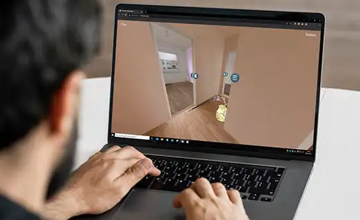 Blick über die Schulter auf einen Laptop: Im Browser wird die virtuelle Wohnung mit interaktiven Markierungspunkten dargestellt.