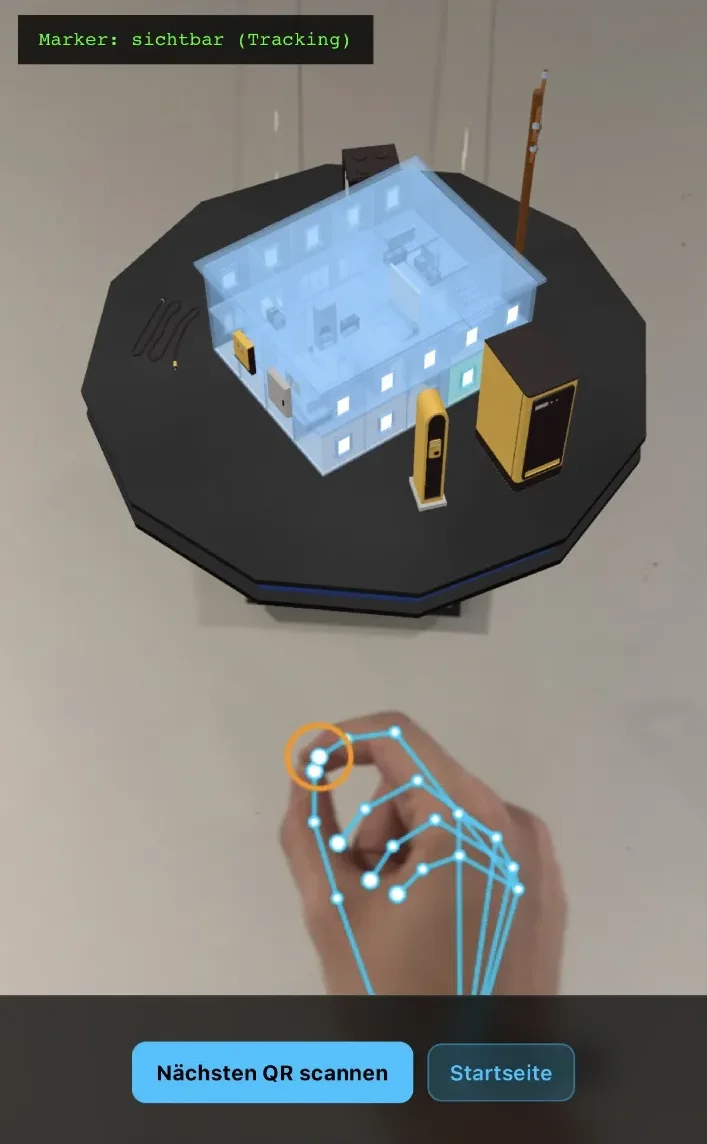 Smartphone-Ansicht der AR-Anwendung: Über einem realen Raum schwebt ein holografisches Hausmodell auf einem dunklen Sockel, darunter wird eine per Handtracking erkannte Hand mit blauen Gelenkpunkten dargestellt. Oben die Statusanzeige „Marker: sichtbar (Tracking)“.